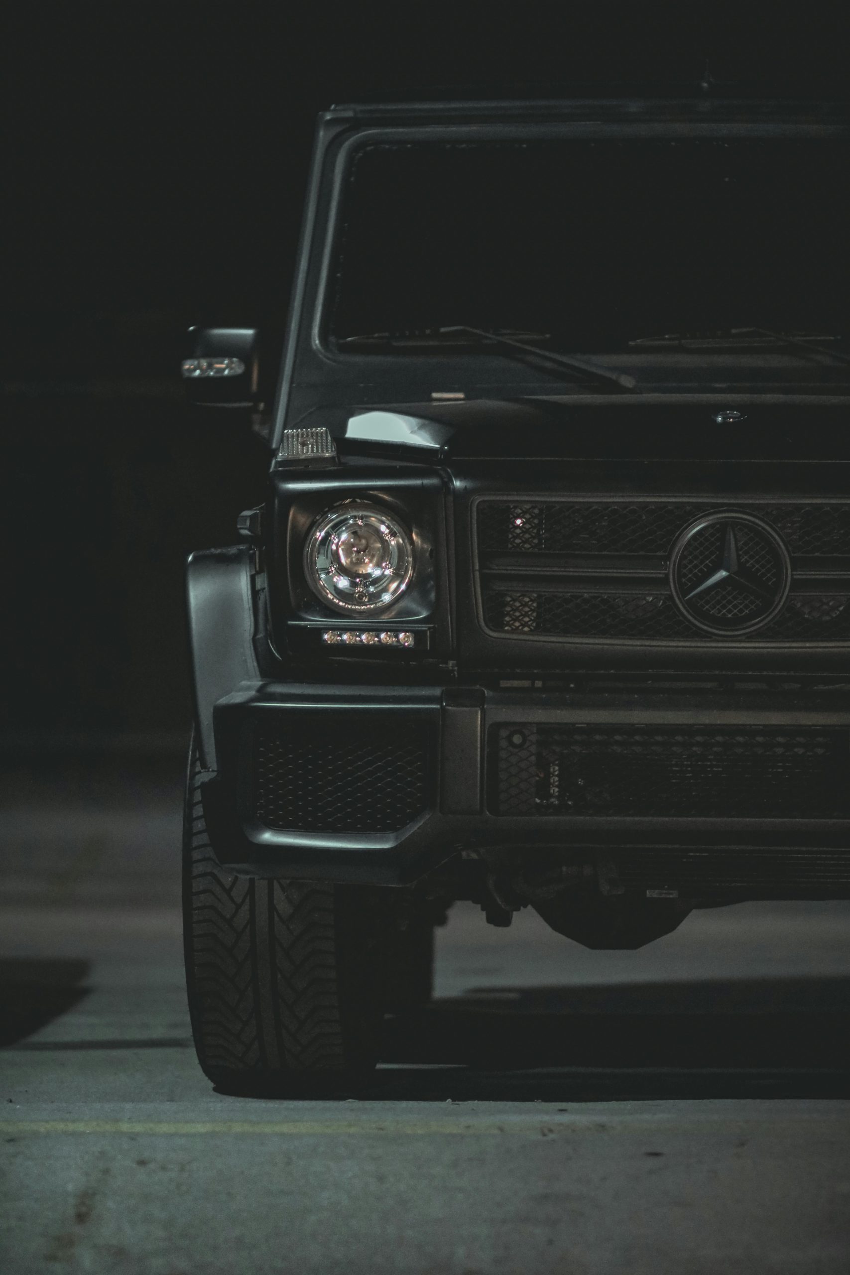 Close-up of a luxury black car's front, featuring a sleek design and emblem under nighttime lighting.